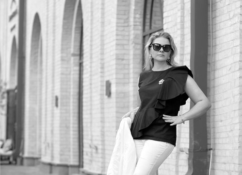 Black and white photo elegant business woman in sunglasses in a stylish black blouse and white trousers on a summer morning on a city street. Business lady. Copy space on the left