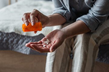 cropped view of woman with menopause holding bottle and pouring pills in hand.