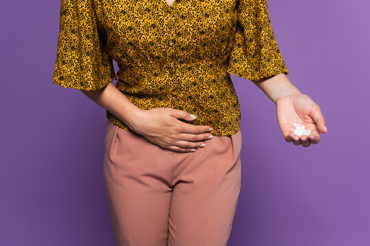 cropped view of woman with stomach ache holding pills isolated on purple.
