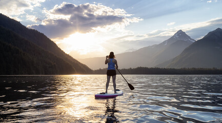 Adventurous Woman Paddle Boarding in a Lake around Canadian Mountain Landscape. Chilliwack Lake, British Columbia, Canada. Adventure Sport Travel