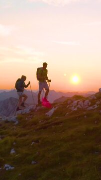 AERIAL, LENS FLARE: Carefree young trekkers on an active summer vacation hiking uphill on a picturesque summer morning. Tourist couple exploring the stunning Julian Alps at sunrise. Fun recreation.