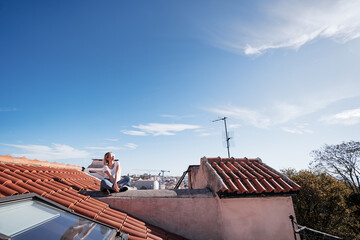 Happy young woman sitting on red tiled roof.