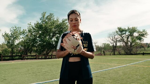 A wide gimbal shot of a female softball athlete posing with her baseball glove on a practice field.  She stares intently into the camera producing an epic atmosphere. Shot in glorious slow motion.