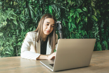 A young girl with a prosthetic bionic arm is studying or working on a laptop against a wall of...