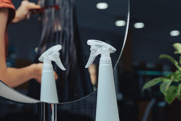 A spray bottle for moisturizing hair stands in front of a mirror in a hairdressing salon