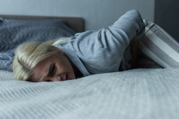 stressed woman lying on bed while feeling pain in stomach during menopause.
