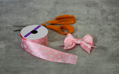 A pink bow with clip  for little girl's hair and view of pink ribbon with white polka dots and scissors on the background.