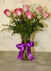 A bicolored roses flower arrangement in a glass vase with purple ribbon.
