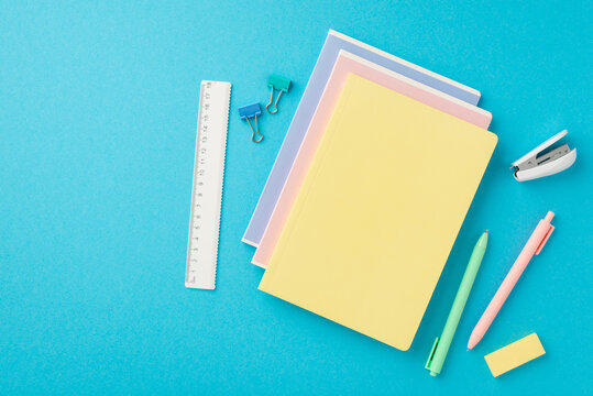 Back to school concept. Top view photo of colorful stationery stack of notebooks mini stapler pens eraser ruler and binder clips on isolated blue background