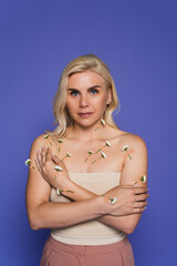 Fototapeta premium blonde woman with plasters and fresh flowers on body looking at camera isolated on purple.