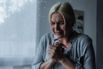 depressed blonde woman crying behind window glass with rain drops.