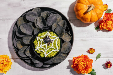 Spooky Halloween black potato chips with guacamole dip: appetizer into a Halloween with of black olive spider