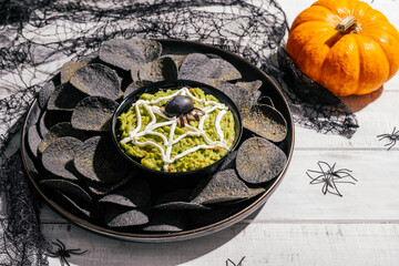 Spooky Halloween black potato chips with guacamole dip: appetizer into a Halloween with of black olive spider