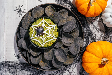 Spooky Halloween black potato chips with guacamole dip: appetizer into a Halloween with of black...