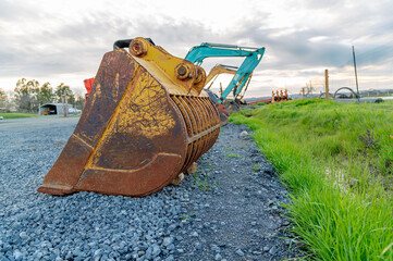 Old rusty excavator bucket close-up. Many excavators in the parking lot. Green grass on the...