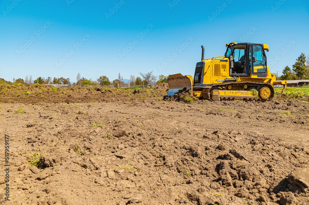 Wall mural sidet view of a yellow bulldozer on a plot of land. a bulldozer clears the area. blue sky background