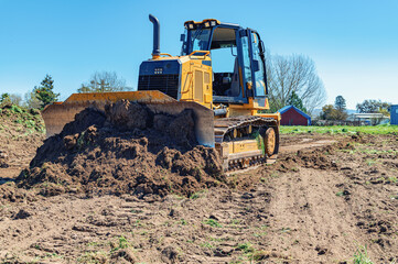 Working bulldozer clears the area before construction. Blue sky background. - obrazy, fototapety, plakaty