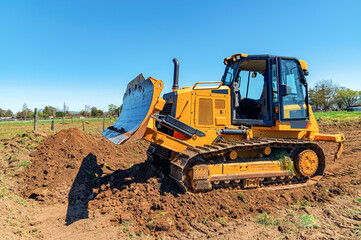 Side view working bulldozer clears the area before construction. Blue sky background. - obrazy, fototapety, plakaty
