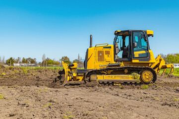 Obraz premium Side view working bulldozer clears the area before construction. Blue sky background.