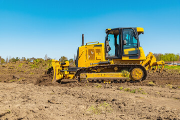 Side view working bulldozer clears the area before construction. Blue sky background. © Vitalii