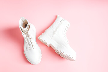White demi-season boots made of eco-leather with fasteners, laces and rough soles on a pink.