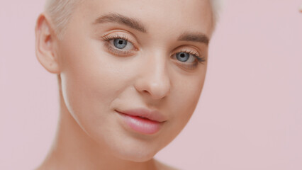 Beautiful young slim blonde Caucasian woman smiles for the camera on pale pink background | Body hydration concept