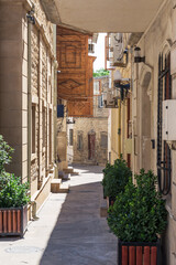 Stone carving decorated houses on narrow alley in old town with green bushes, Baku, Azerbaijan