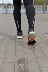 Fototapeta na wymiar Legs of a person running on the cobblestones. The man is running. Sportswear. Healthy lifestyle. Wet footprints from shoes on the dry surface of the track.