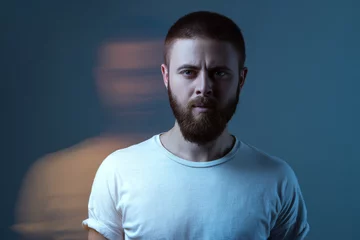 Double exposure crative portrait of artistic bearded model man in white t-shirt looking at camera with calm serious face. special blurred beauty effect. indoor studio shot. © khosrork