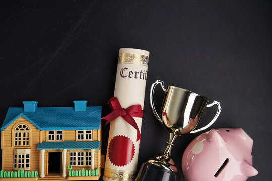 trophy certificate piggy bank and model house on blackboard