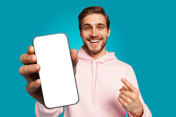 Handsome Excited Man Showing Pointing At Empty Smartphone Screen Posing Over Light Blue Background, Smiling To Camera