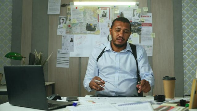 Frustrated detective smoking and thinking about investigation. Black male cop looking through the documents, smoking a cigarette and leaning back in chair in police department.High quality 4k footage