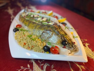 whole fish baked pike perch on a white platter is served in the restaurant