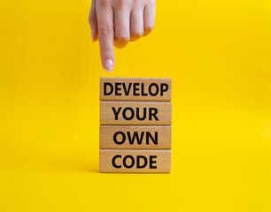 Develop your own code symbol. Concept words Develop your own code on wooden blocks. Beautiful yellow background. Businessman hand. Business and Develop your own code concept. Copy space.