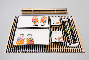 Sushi kit with plates with oriental illustration, chopsticks and a sushi mat, isolated on white