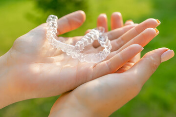 Close up womans hand holding invisible aligners for whitening and straightening of teeth on the green background. Orthodontic therapy after brackets. Teeth healthcare