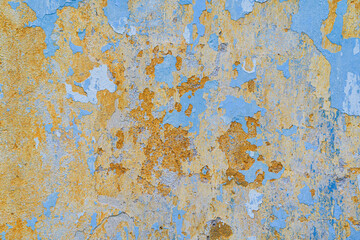 Fragment of a wall with old plaster. Traces of layers of paint of different colors are visible on the surface. Blue and yellow. Background. Texture.