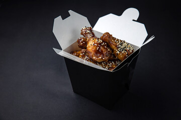 fried chicken wings with sauce and cheese in a delivery box on a black background
