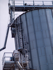Naklejka premium Modern elevator for grain storage. A large plant for the storage and processing of grain crops, view of the granary on a cloudy day. Agro manufacturing plant for processing and drying