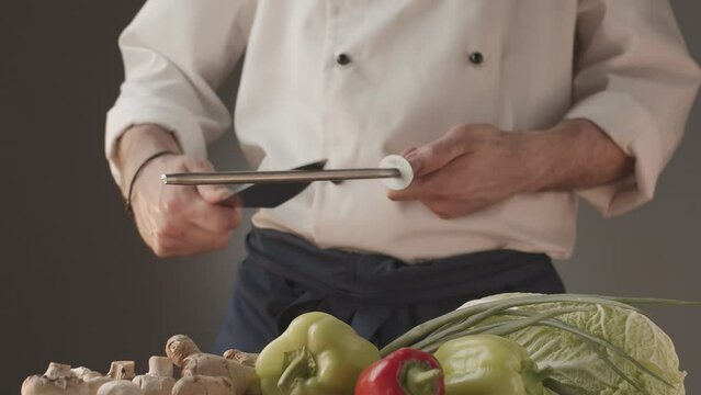 Close up shot of chef sharpening a cool knife before cutting meat or making a meal. Professional cooker preparing an instrument for work. Cook sharpens knife on knife on domestic kitchen.