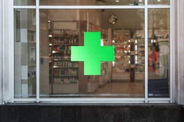 Green cross sign with neon light mounted on pharmacy shop window case outdoor - obrazy, fototapety, plakaty