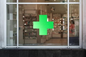 Fotobehang Green cross sign with neon light mounted on pharmacy shop window case outdoor © Bonsales