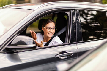 A young woman is sitting in her car in traffic and talking to another driver in the car. She respects traffic regulations. A girl in a car in traffic