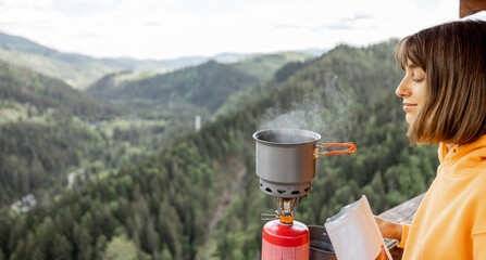 Young woman prepares freeze-dried food for hiking in airtight package, boiling water with gas...