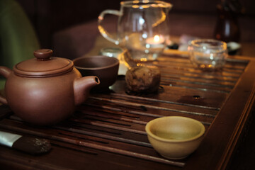 Fototapeta na wymiar Traditional chinese tea ceremony utensils on a tea tray. Chinese teapots made of brown yixing clay and glass and cups. Tea brewing equipment low key dark mood