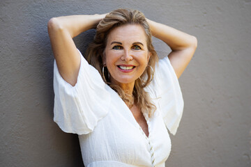 Attraktive Frau mit sympathischem Lächeln in einem Sommerkleid vor einer grauen Wand 