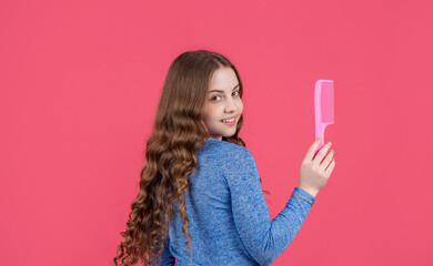 positive teen girl with curly hair hold comb on pink background