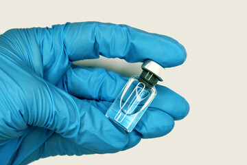 A hand in a blue medical glove close-up holding a vaccine against a light background. The concept...
