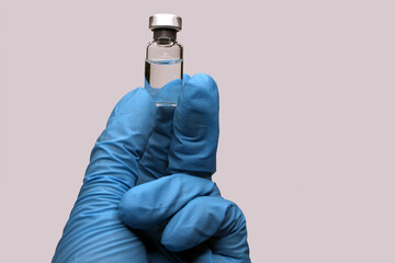 A hand in a blue medical glove close-up holding a vaccine against a light background. The concept...