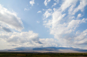 Fototapeta premium Fields and meadows with young vineyards and apricot orchards in the Ararat valley in the foot of mount Ararat in the distance hidden by clouds